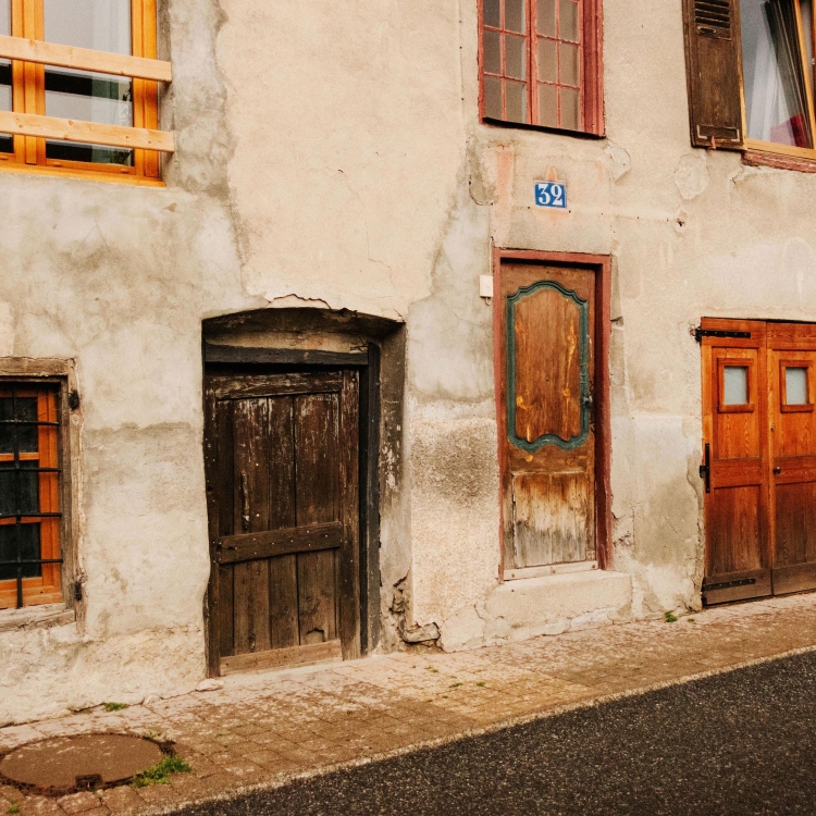 Exterior view of a weathered building facade featuring aged wooden doors and windows, showing a rustic and vintage architectural design.
