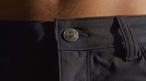 Close-up of a man's black trousers with a branded button, showcasing fashion and attention to detail in an indoor setting.