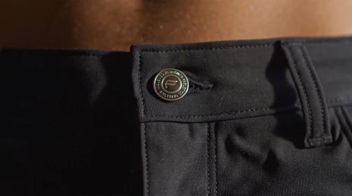 Close-up of a man's black trousers with a branded button, showcasing fashion and attention to detail in an indoor setting.