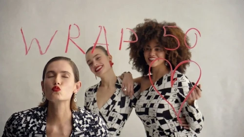 Three women in patterned tops pose in front of a white background with hand-drawn text and a heart. Red lipstick and jewelry are visible.