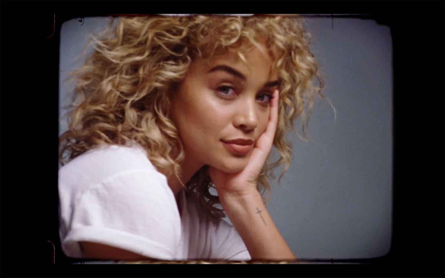 Portrait of an adult woman with blonde curly hair in a white shirt posing against a gray backdrop with shallow depth of field.