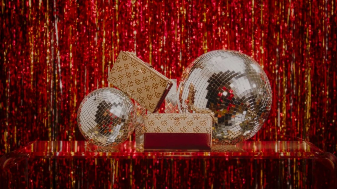 Studio shot of two patterned handbags and two disco balls on a reflective surface against a red glitter background. Product photography.