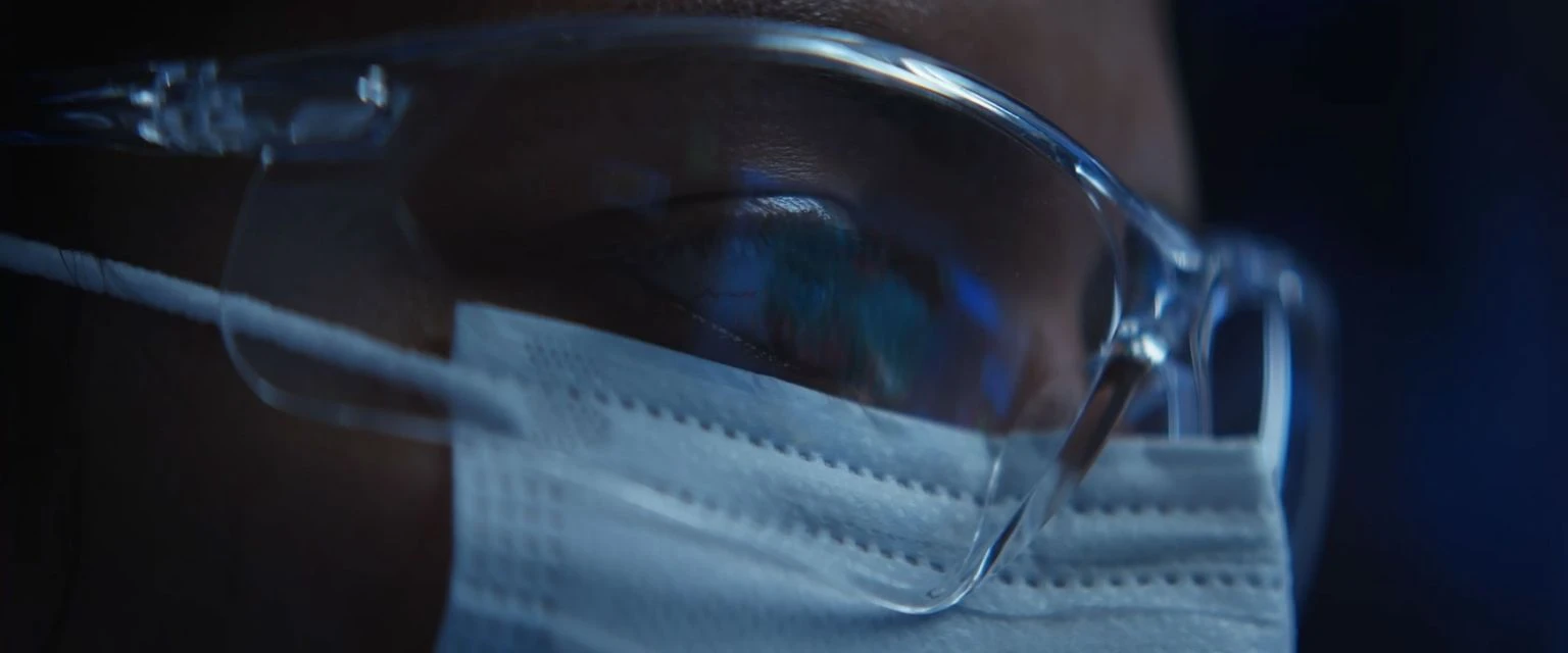 Close-up of face protection: safety glasses and white surgical mask. Medical or industrial safety concept. Dark blue background.