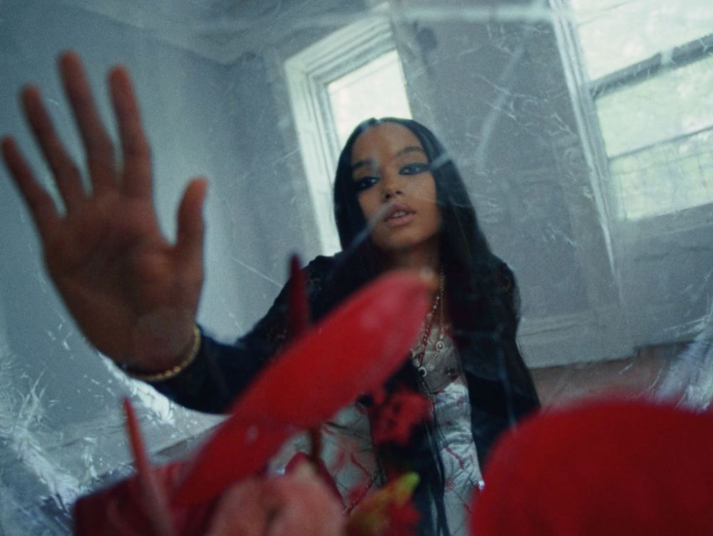 Indoor portrait of a young adult woman with long dark hair with a hand pressed against a surface in a softly lit interior room.