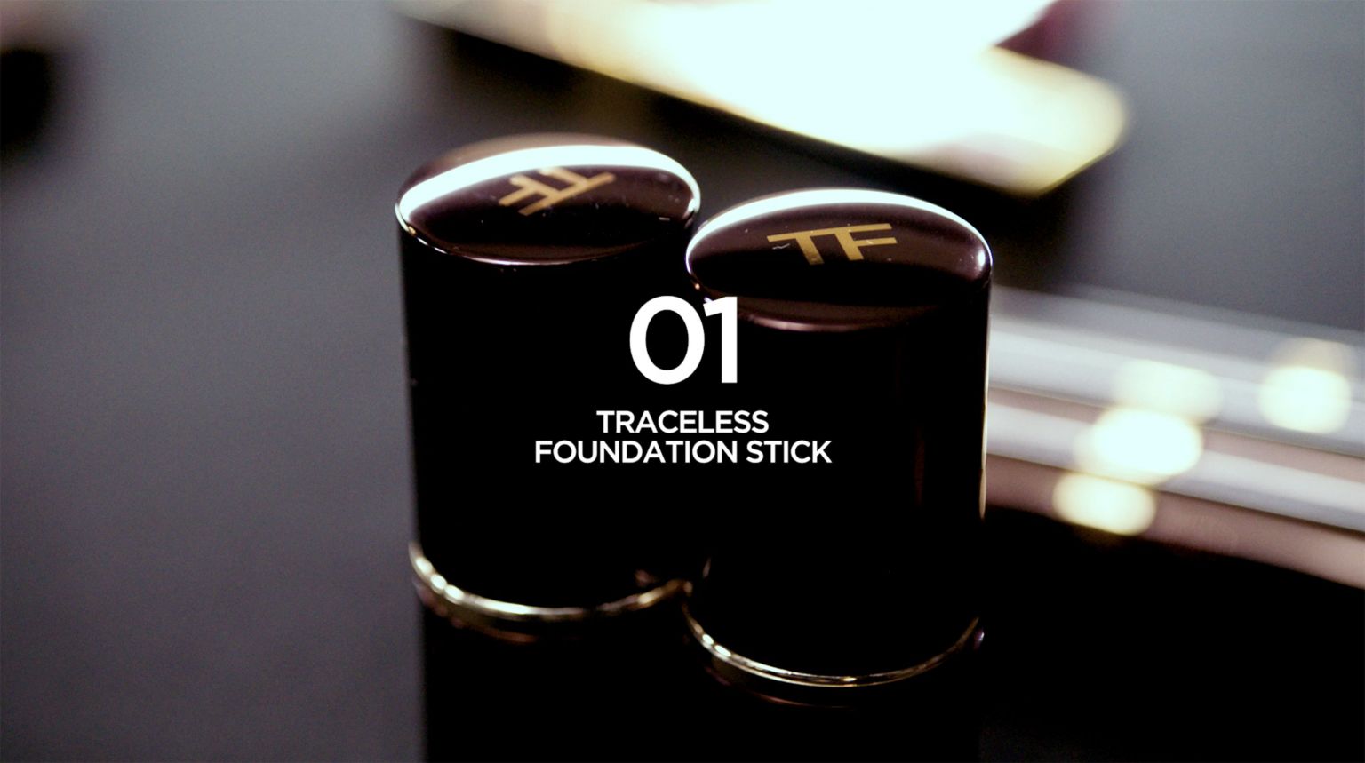 Two dark foundation sticks by Tom Ford are presented in a studio setting with bright white text overlay, highlighting the beauty product.