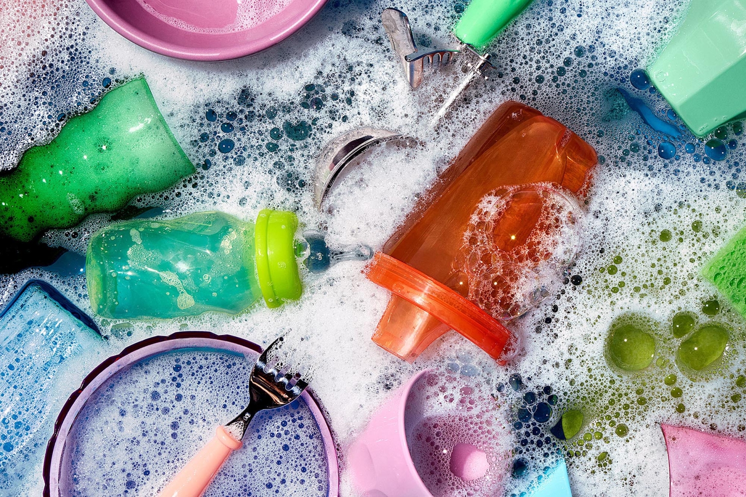 Overhead shot of soapy water filled with colorful baby bottles, sponges, and dishwashing tools, creating a vibrant and clean scene.