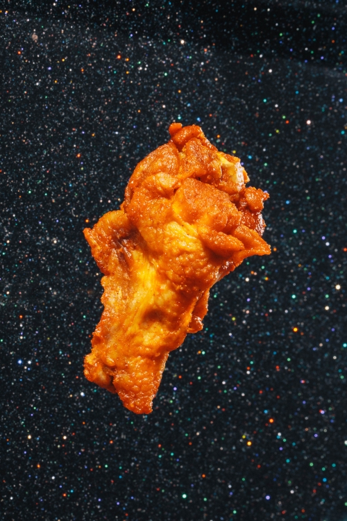 An abstract golden fried food item on a dark blue and black speckled background that resembles a starry night sky.