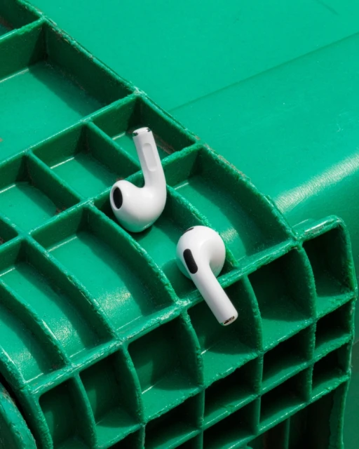 Close-up studio shot of two white wireless earbuds against a green textured surface, minimal and bright, focusing on product details.