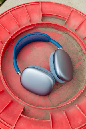 A pair of modern blue and silver headphones sit centered on a red textured surface in an eye-level shot emphasizing sleek audio tech.