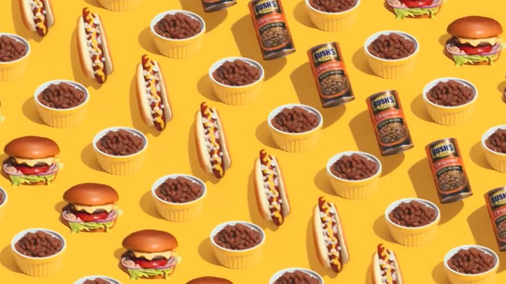 Overhead pattern on yellow backdrop: canned beans, bowls of baked beans, hot dogs with mustard, and cheeseburgers with lettuce and tomato.