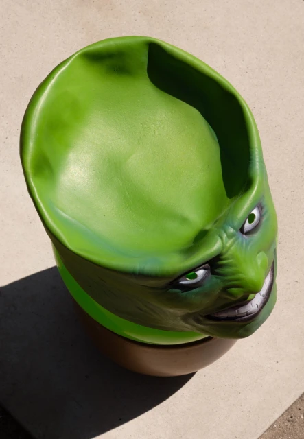 Eye-level shot of green, four-eyed chair with sinister face on a beige surface, capturing its unique design and playful horror vibe.