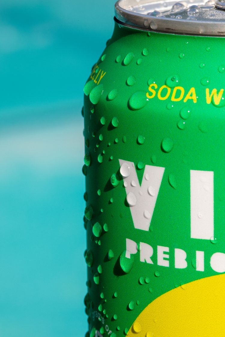Close-up of a green can with water droplets against a blurred turquoise background, highlighting product freshness and visual appeal.