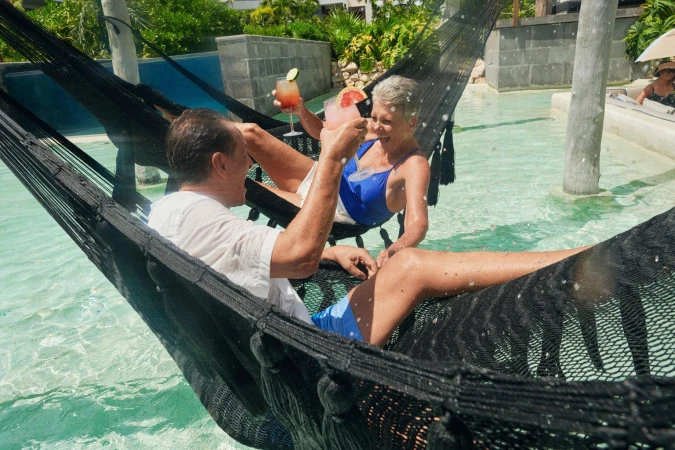 Older couple relaxing in hammocks in a resort swimming pool while enjoying cocktails, soaking up the sun, and enjoying their vacation.