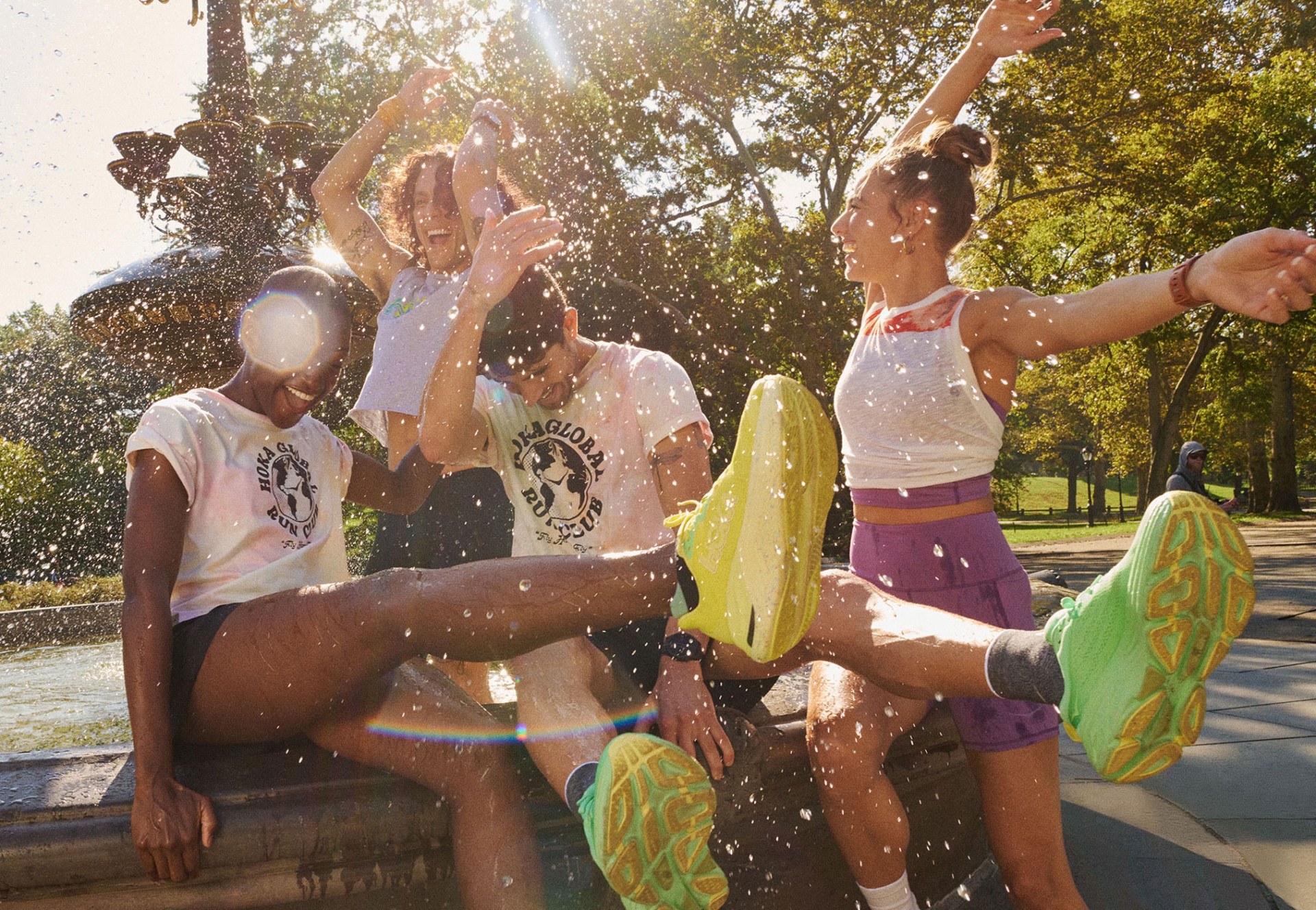 Outdoor shot of a diverse group of young adults in sportswear enjoying a sunny day near a fountain, captured with a wide-angle lens.