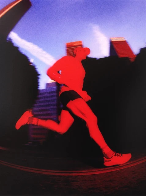 A male runner in motion on a track in an urban setting, rendered in a high-contrast red and blue color palette.