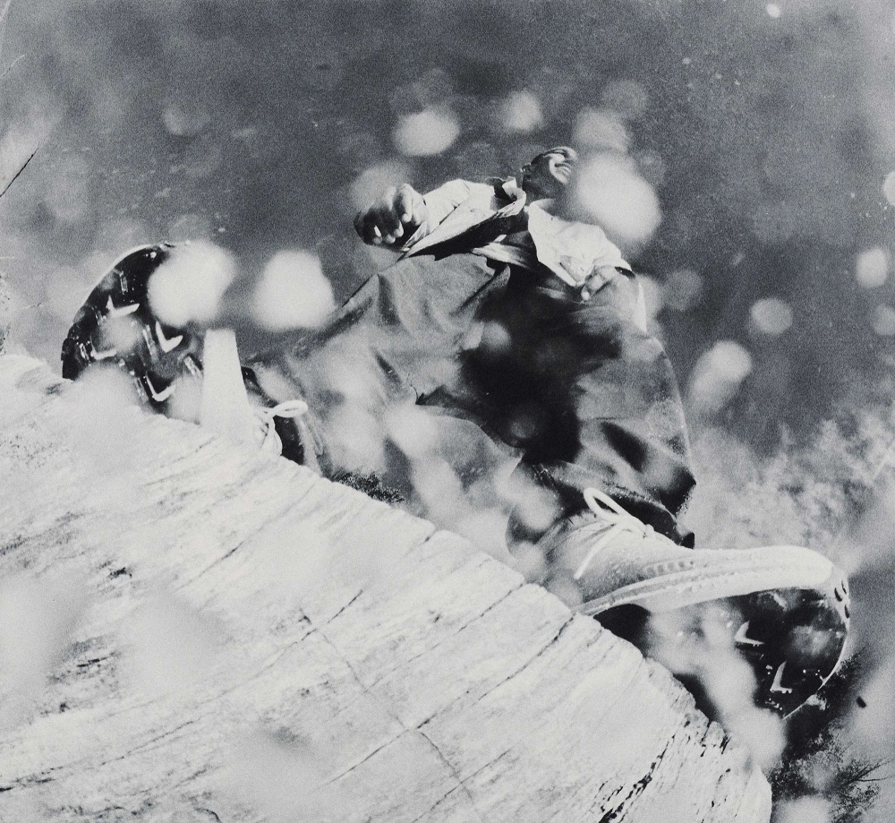 Black and white action shot of a person falling while wearing outerwear and sneakers on a rocky surface with bright bokeh.