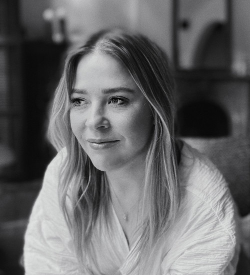 Black and white portrait of a fair-skinned woman with blonde hair wearing a white shirt looking slightly to the right indoors.