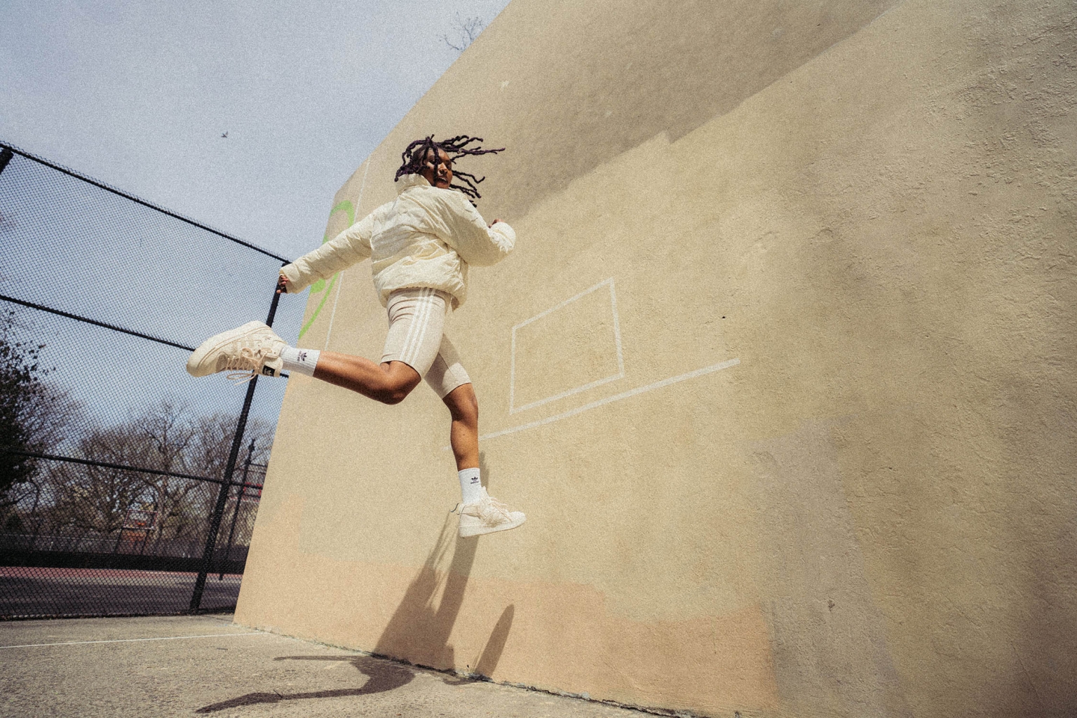 Athletic adult leaps in sporty apparel against a wall on an outdoor court, exuding energy and motion, captured in an eye-level shot.
