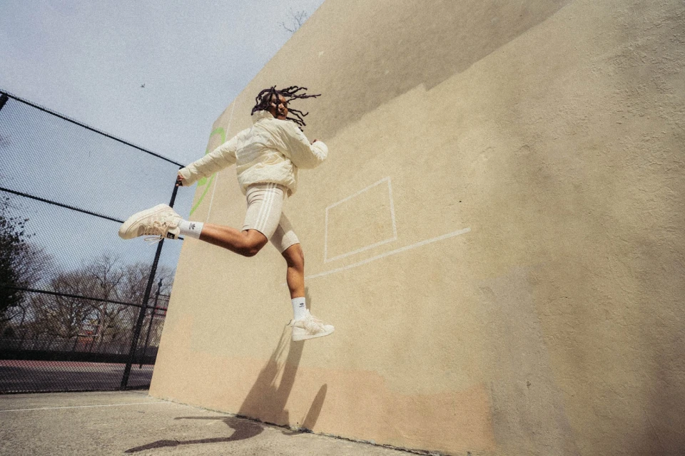 Athletic adult leaps in sporty apparel against a wall on an outdoor court, exuding energy and motion, captured in an eye-level shot.