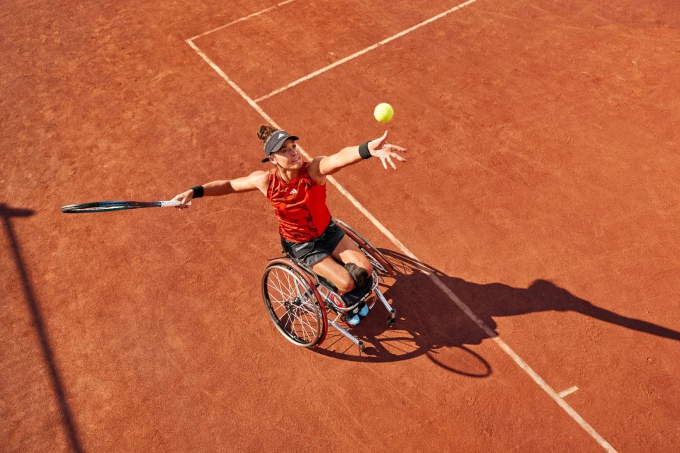 Overhead shot of a female wheelchair tennis player reaching up to serve a tennis ball on a clay court, action and sport.
