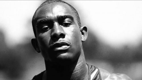 Close-up black and white portrait of an athletic African American man with a determined expression. Outdoors, natural light, athletic wear.
