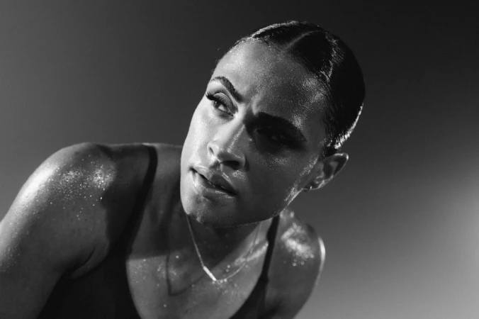 Close-up monochrome portrait of a sweating woman with dark hair pulled back, wearing a thin strap top.
