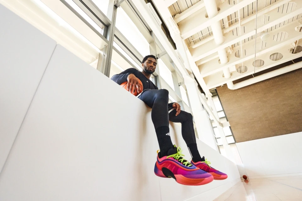 Adult male athlete poses indoors wearing athletic clothing and colorful basketball shoes while holding a basketball at eye level.