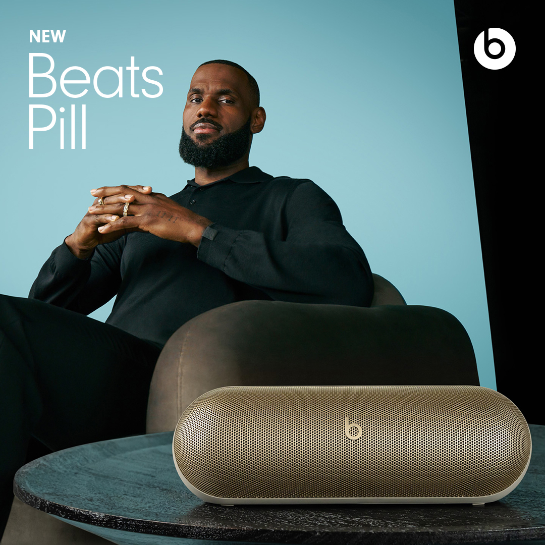 LeBron James poses in a photo studio with a Beats Pill speaker on a table, emphasizing a blend of celebrity and audio technology.