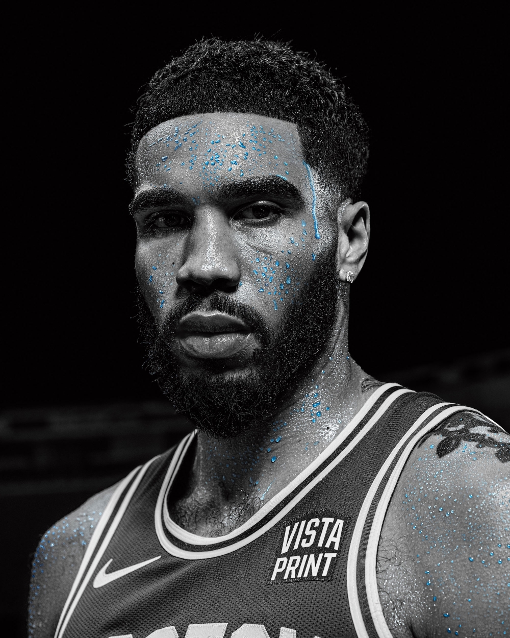 Portrait of a sweaty African-American basketball player in a grey uniform with a focused expression against a dark background.