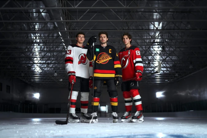 Three male ice hockey players in team jerseys pose on the ice rink, holding hockey sticks, with an indoor stadium visible in the background.