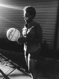 Black woman wearing sunglasses and holding a Spalding basketball outdoors in a high-contrast black and white portrait.