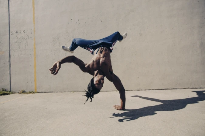Man upside down breakdancing on concrete ground against a plain wall by Marcus Smith