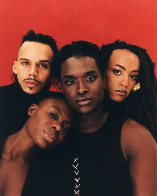 Portrait of four people in studio setting with a red backdrop. Three are posed closely together and one has their head resting.