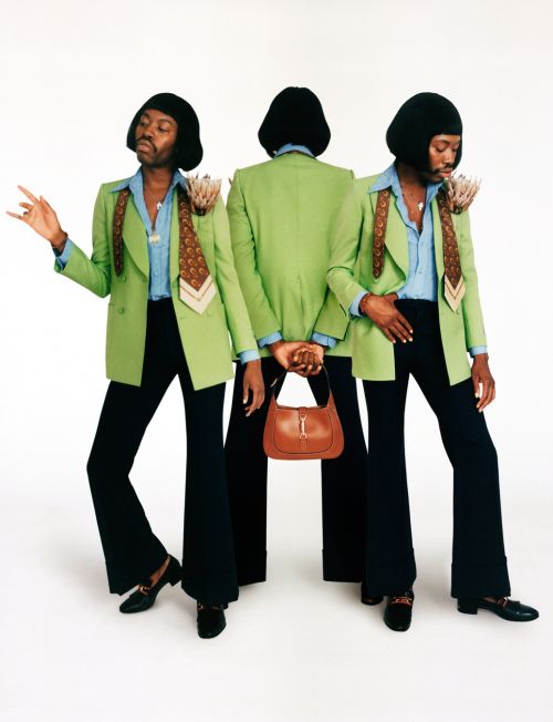 Three adult men in matching green vintage-style suits and bell-bottoms pose with a brown leather purse against a white backdrop.
