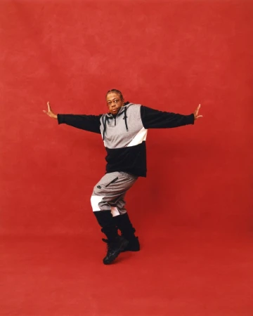 Black man wearing a color-blocked hoodie and sweatpants posing against a red textured backdrop