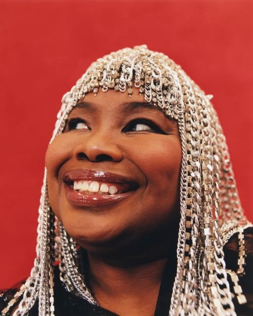 Close-up studio portrait of a smiling African-American woman wearing silver chain headwear and a black top against a red backdrop.