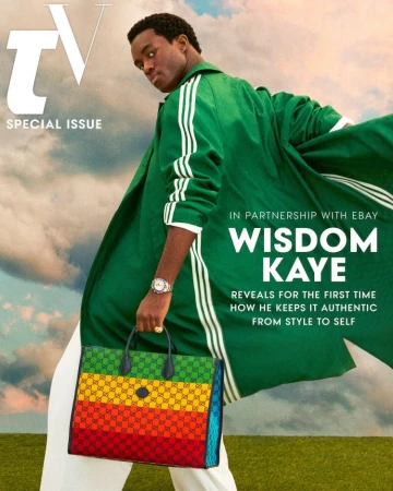 Wisdom Kaye wearing a green jacket with white stripes, holding a multicolored striped handbag against a cloudy sky
