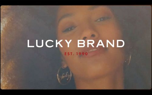 Close up of an adult woman with curly hair, jewelry, and a clear view of the Lucky Brand logo and the company's founding date.