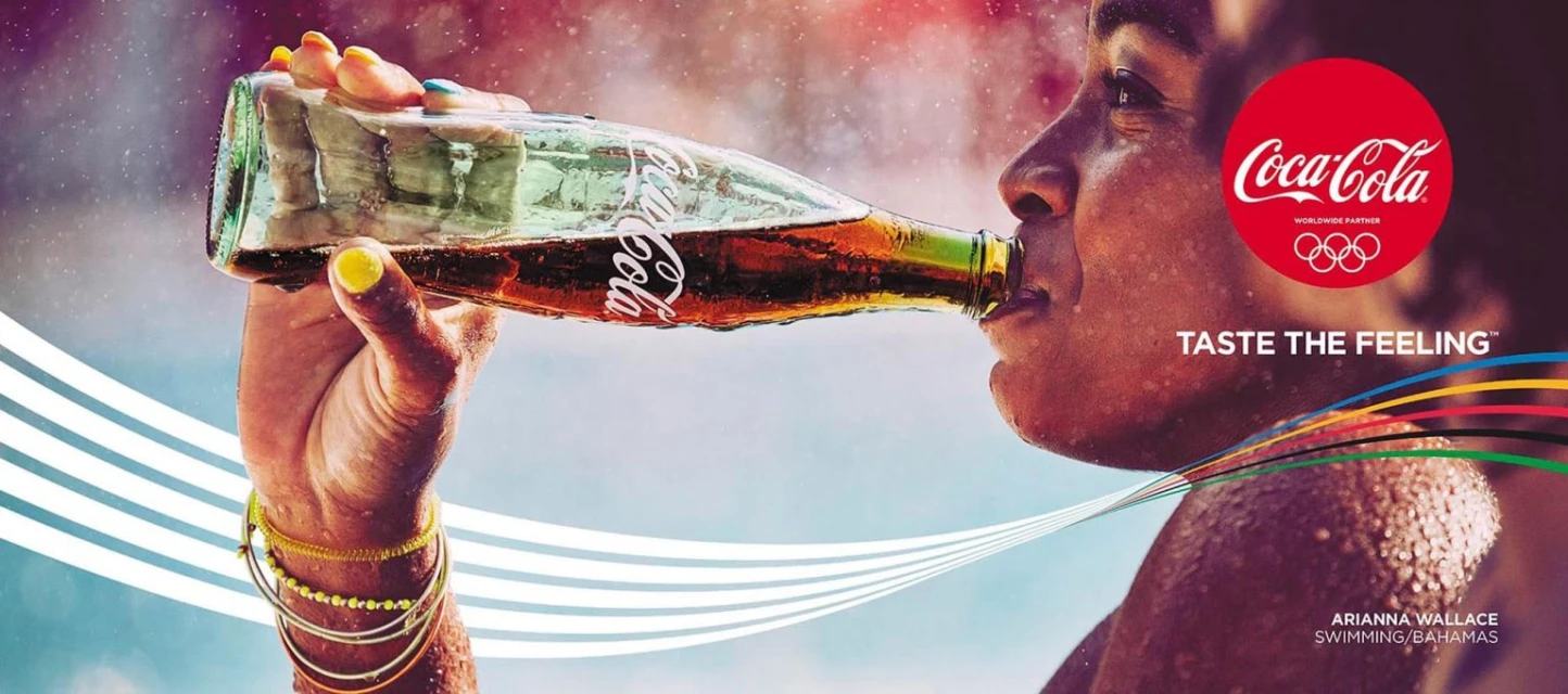 A woman drinks from a glass Coca-Cola bottle in an ad featuring the Olympic logo and a vibrant, summery color palette.
