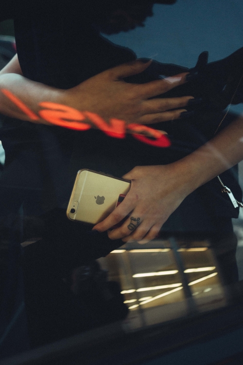 Close-up of an adult's arms and hands, with an Apple iPhone in hand, showcasing a glimpse of a tattoo and window reflections.