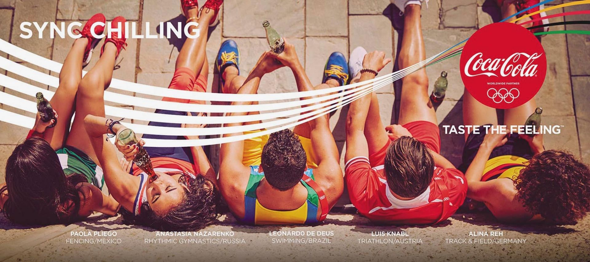 Overhead view of six young adults relaxing on the ground, holding Coca-Cola bottles, promoting 'Sync Chilling' with Olympic rings logo.
