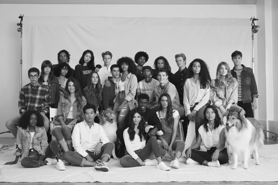 Group portrait in black and white featuring a diverse group of young adults and two collie dogs, posed in front of a white backdrop.