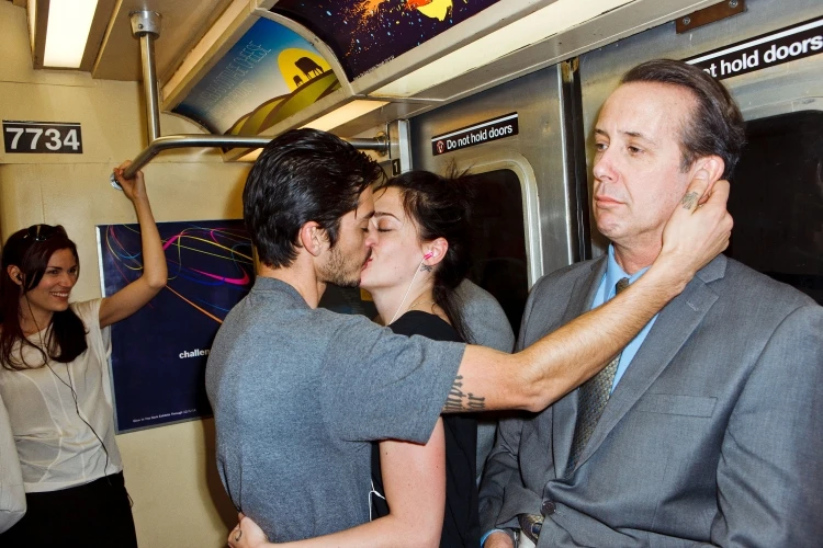 Romantic scene on a subway featuring a kissing couple, woman with earphones, and a man in a suit looking with a serious expression.