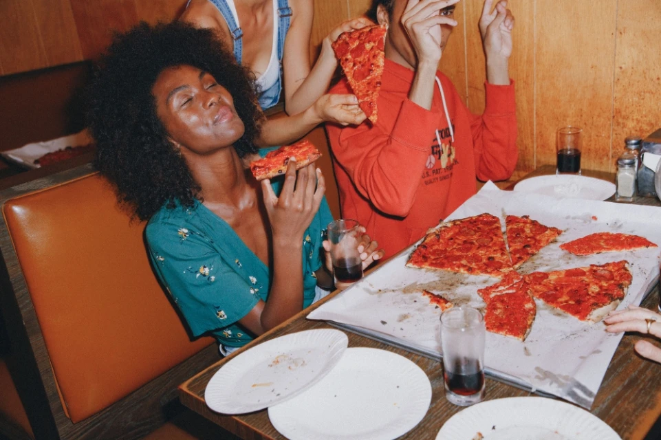 Three young adults enjoy pepperoni pizza in a vintage diner, with warm lighting and casual fashion, capturing a relaxed and social scene.