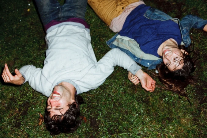 Two people lying on grass holding hands, photographed by RJ Shaughnessy in Los Angeles.