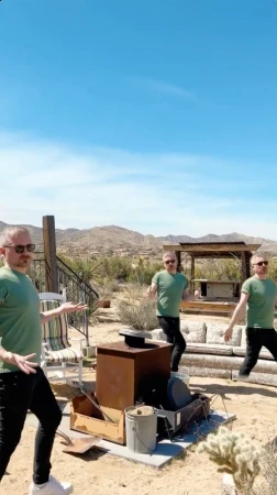 Three digitally cloned adult males in a desert backyard with arid landscape, wearing sunglasses, green shirts, and black jeans, dance.