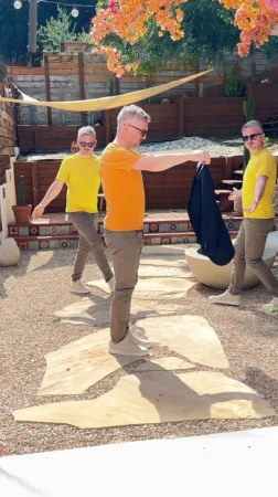 Adult male clones strike a pose on a stone-paved patio. Each man wears a differently colored shirt and dark blazer slung over the shoulder.