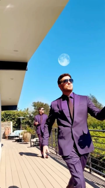 Two adult men in purple suits walk on a wooden deck with a bright blue sky and the moon visible in the background on a sunny day.