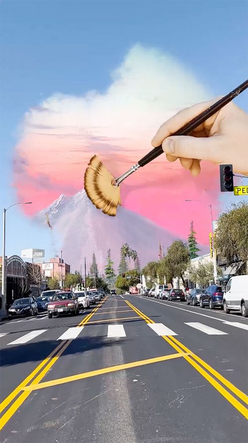 Surreal art of a road leading to a mountain backdrop being painted by a hand holding a brush, merging cityscape with a painted landscape.