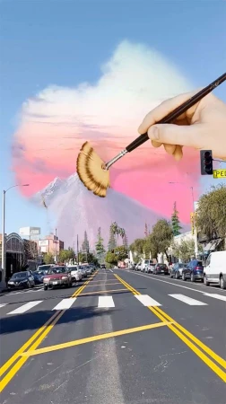 Surreal art of a road leading to a mountain backdrop being painted by a hand holding a brush, merging cityscape with a painted landscape.